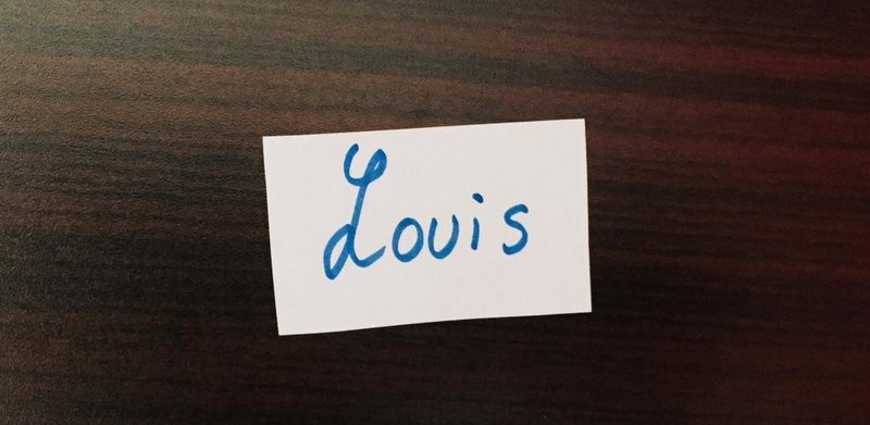White card on a wooden table, with the name “Louis” handwritten on it