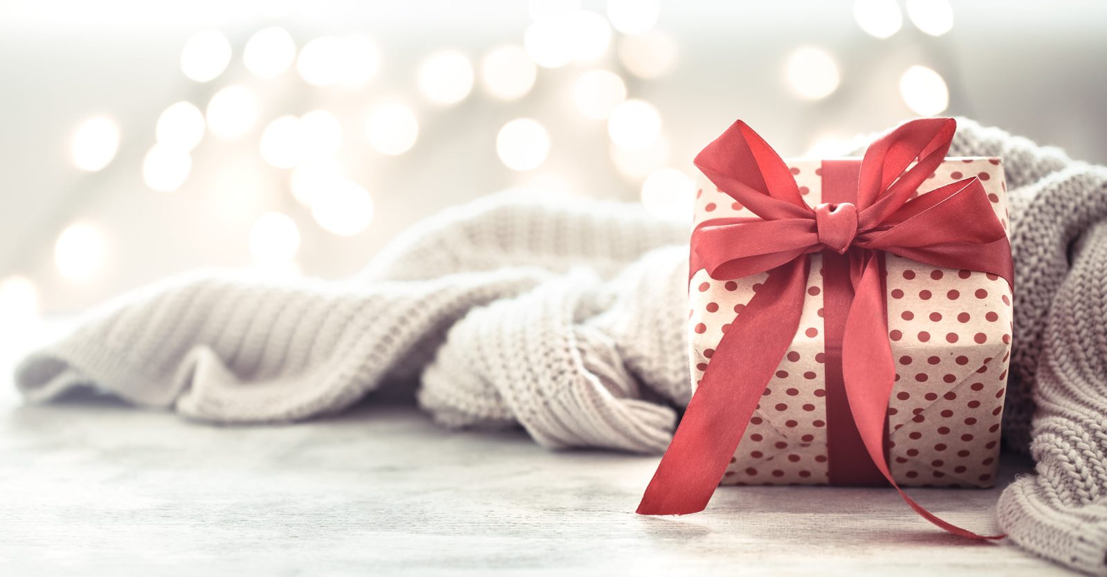 Paquet cadeau à pois noué d'un ruban rouge, posé sur un plaid en laine