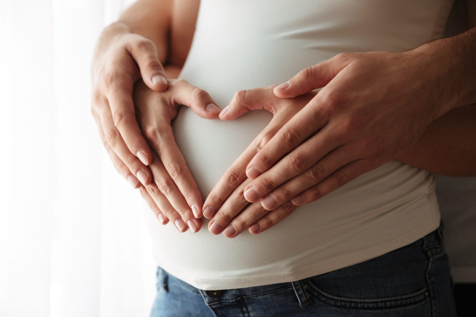 A couple’s hands forming a heart on a pregnant woman’s rounded belly