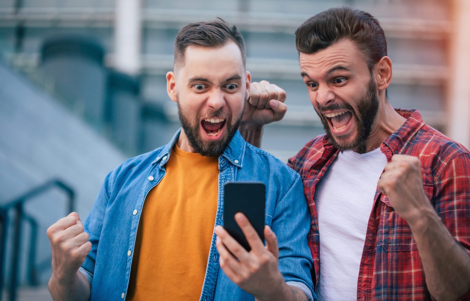 Two bearded friends staring at a smartphone and shouting with joy, fists clenched